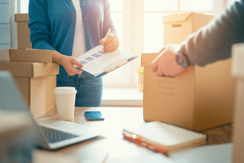 Woman holding a clipboard and man lifting a box from a table with business papers at A-American Self Storage in Santa Fe Springs, California