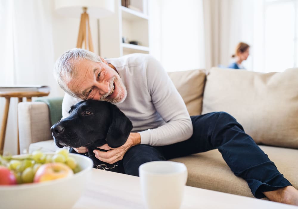 Man petting his dog on the couch at Fairbrooke Senior Apartments in Aberdeen, Maryland