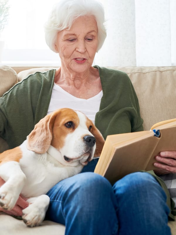 Resident with her dog reading a book on the couch in their senior apartment at West Park Senior Living in San Dimas, California