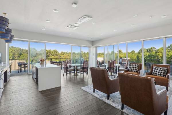 Spacious living room in an active adult community unit with large windows and a balcony view overlooking wooded scenery.