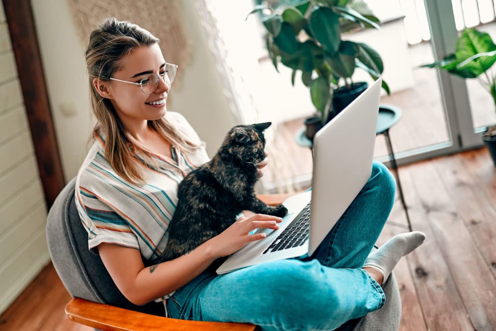 Happy resident and her cat surfing the web on a laptop in their new home at Oaks White Rock in Dallas, Texas