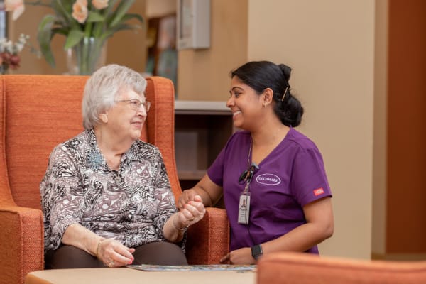 Resident sitting beside caretaker in red furniture at Touchmark at The Ranch in Prescott, Arizona