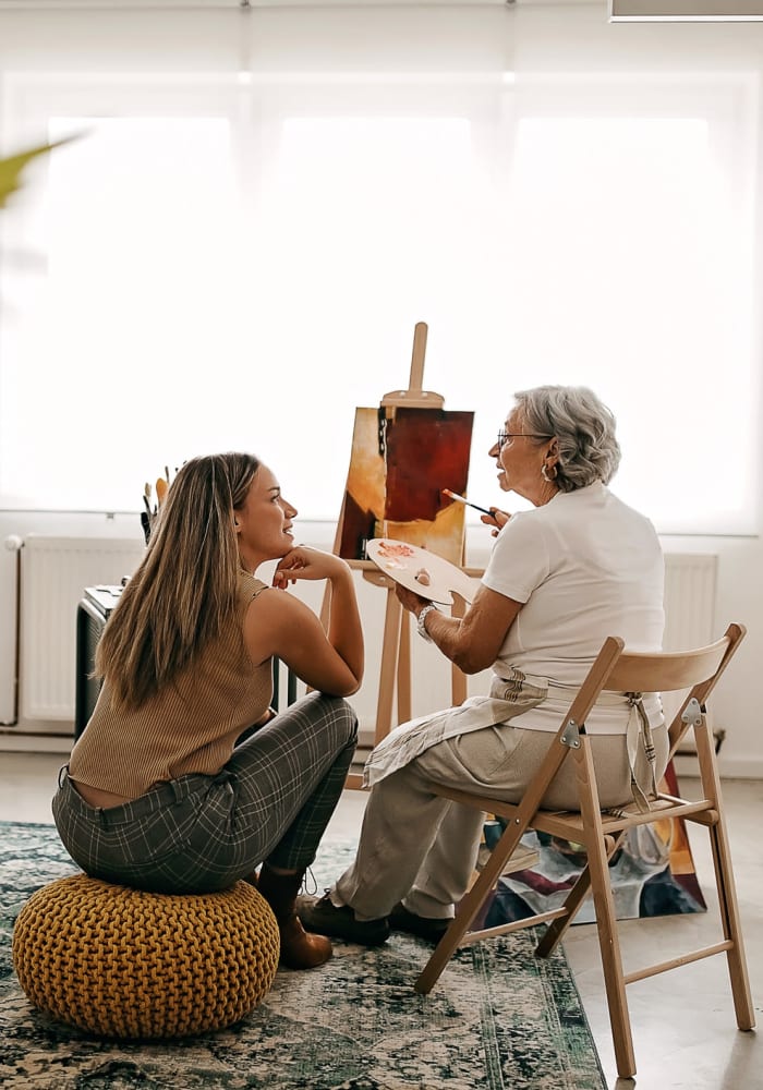 A young woman helping an elderly woman paint at Harbor Cove Memory Care in Hilton Head Island, South Carolina