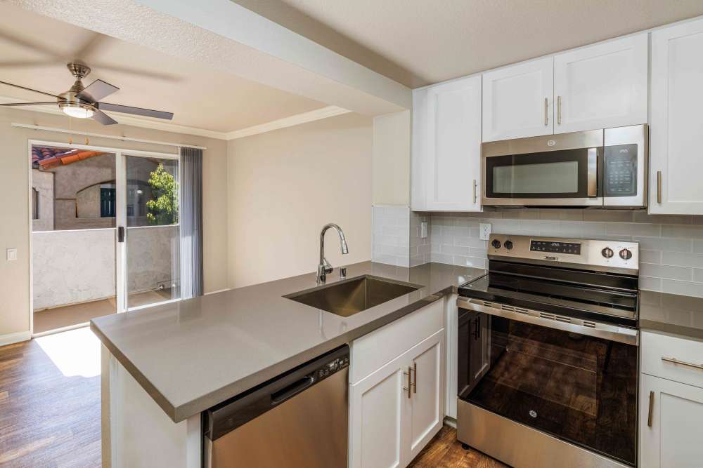 Kitchen with white cabinets, quartz counters & stainless steel appliances, overlooking the dining room and balcony.