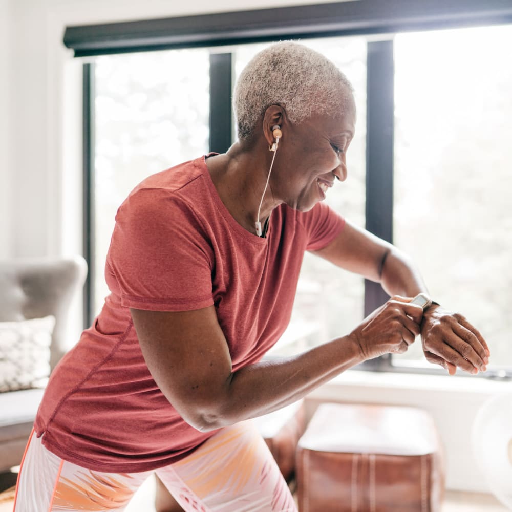 Resident checking her pulse on a smartwatch as she exercises in her apartment at our Village Green Senior community at Mission Rock at Sonoma in Sonoma, California