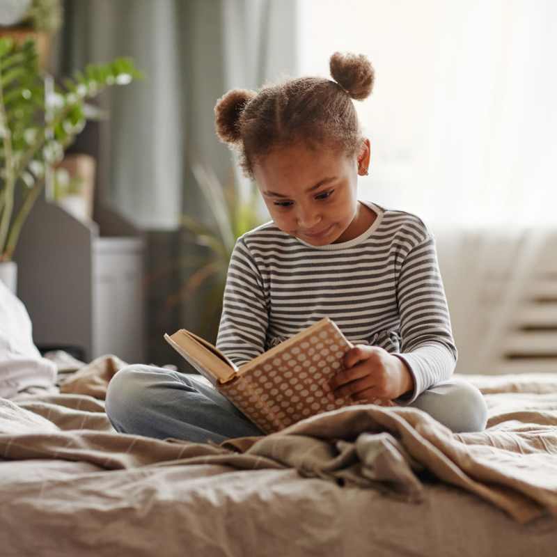 A young girl reads a book on her bed at Attain at Quarterpath, Williamsburg, Virginia