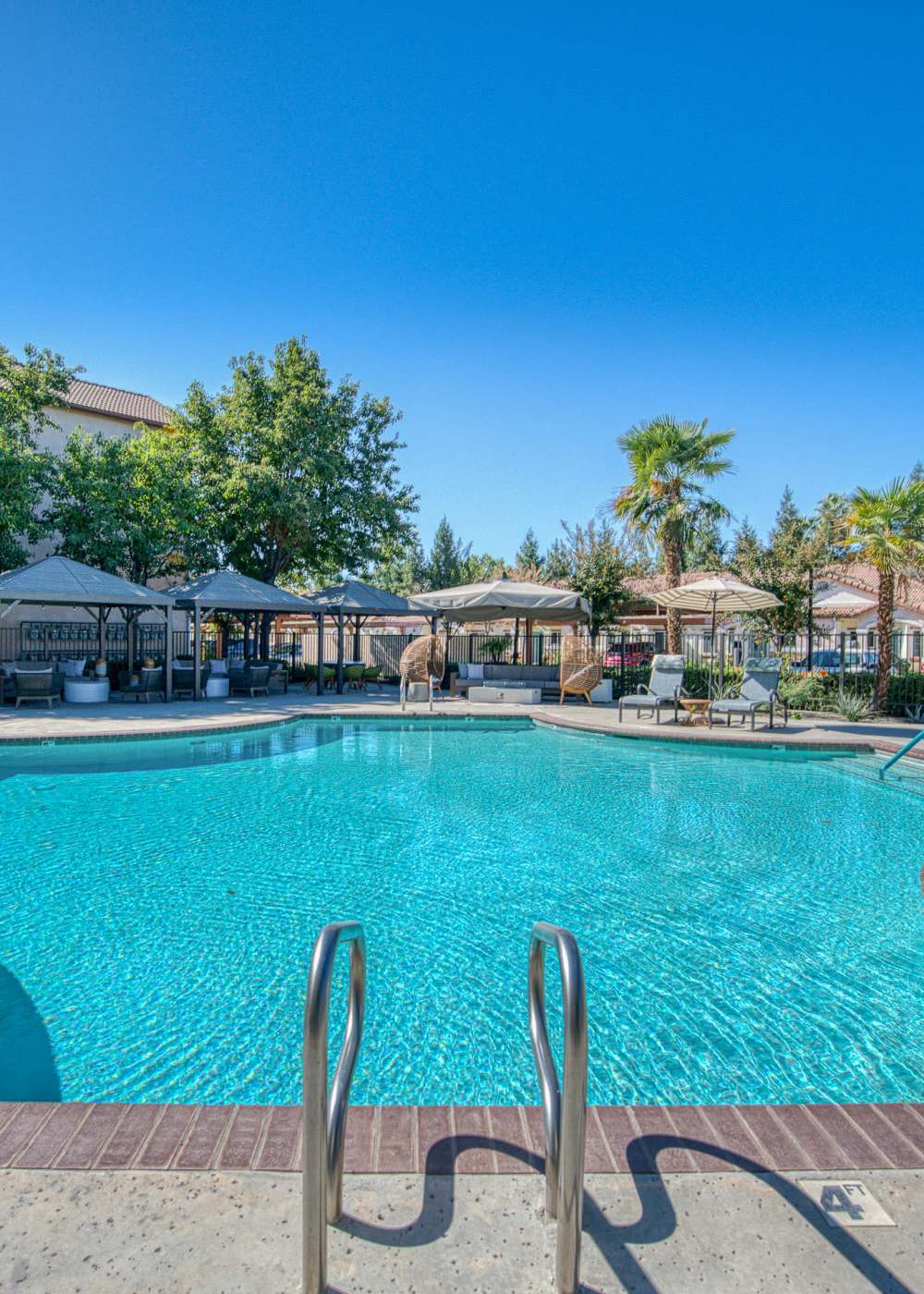 Sparkling resort-style pool surrounded by shaded cabanas and lounge chairs under clear blue skies at Westwood Bluffs in Fresno, California