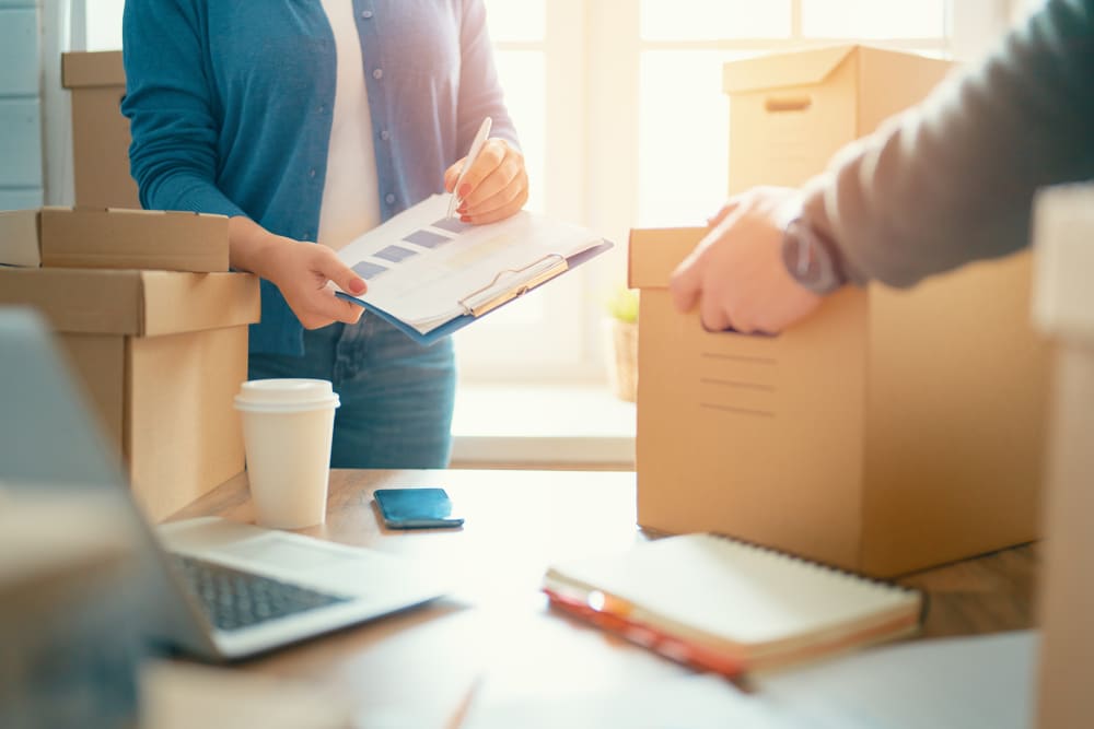 Woman holding a clipboard and man lifting a box from a table with business papers at A-American Self Storage in Ridgecrest, California