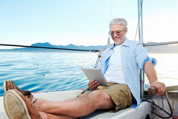 Man sitting on sailboat while looking at tablet