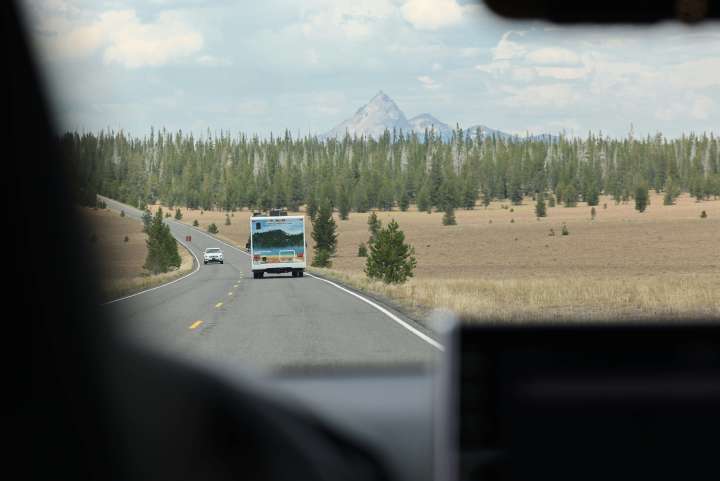 view of the road ahead from the point of view of an RV driving on the road. There are cars in front and in the opposite lane, with trees and a mountain in the background on the road ahead