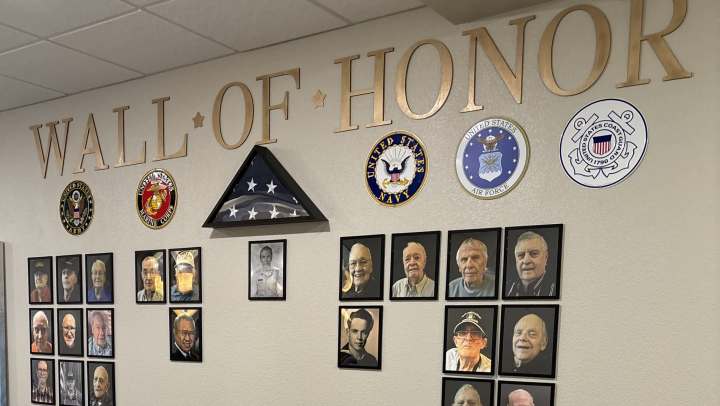 The Wall of Honor at The Landing at Frisco features framed veteran portraits, military emblems, and a folded American flag.