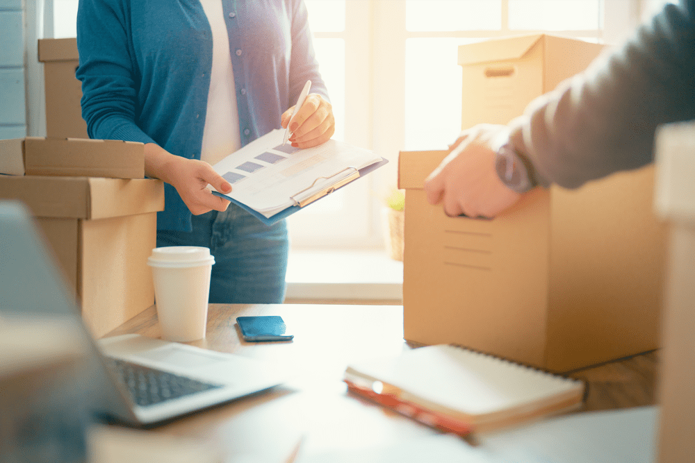 Woman holding a clipboard and man lifting a box from a table with business papers at A-American Self Storage in El Cajon, California