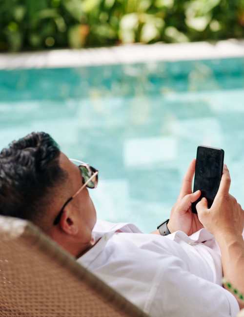 Resident using their mobile phone while relaxing by the pool at Norco Valley Square in Norco, California