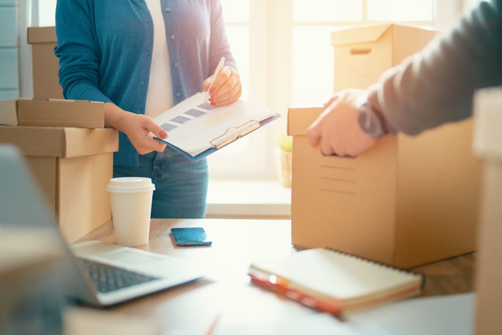 Woman holding a clipboard and man lifting a box from a table with business papers at Sierra Vista Mini Storage in Bakersfield, California