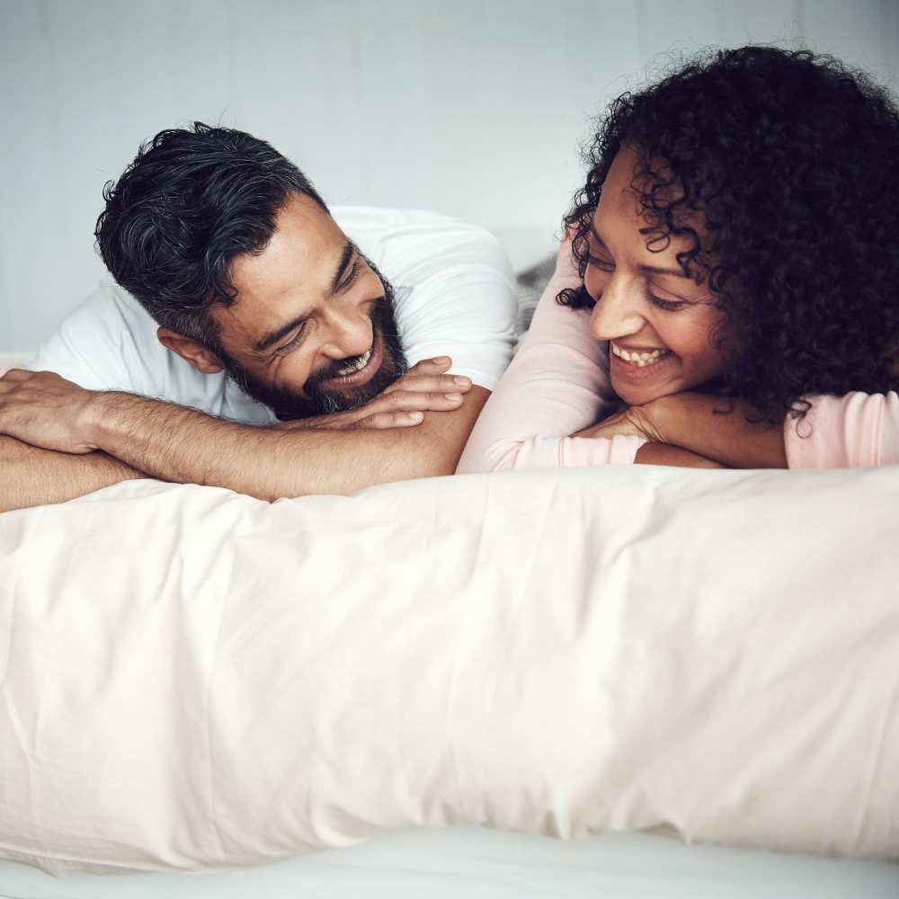 A happy resident couple lying on bed in their apartment home at The Heyward Apartments in Corinth, Texas