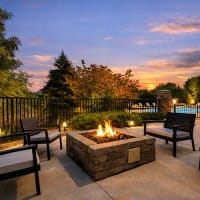 Cozy fire pit surrounded by seating with lush greenery and a sparkling pool in the background at 43 North Apartments in Grand Haven, Michigan