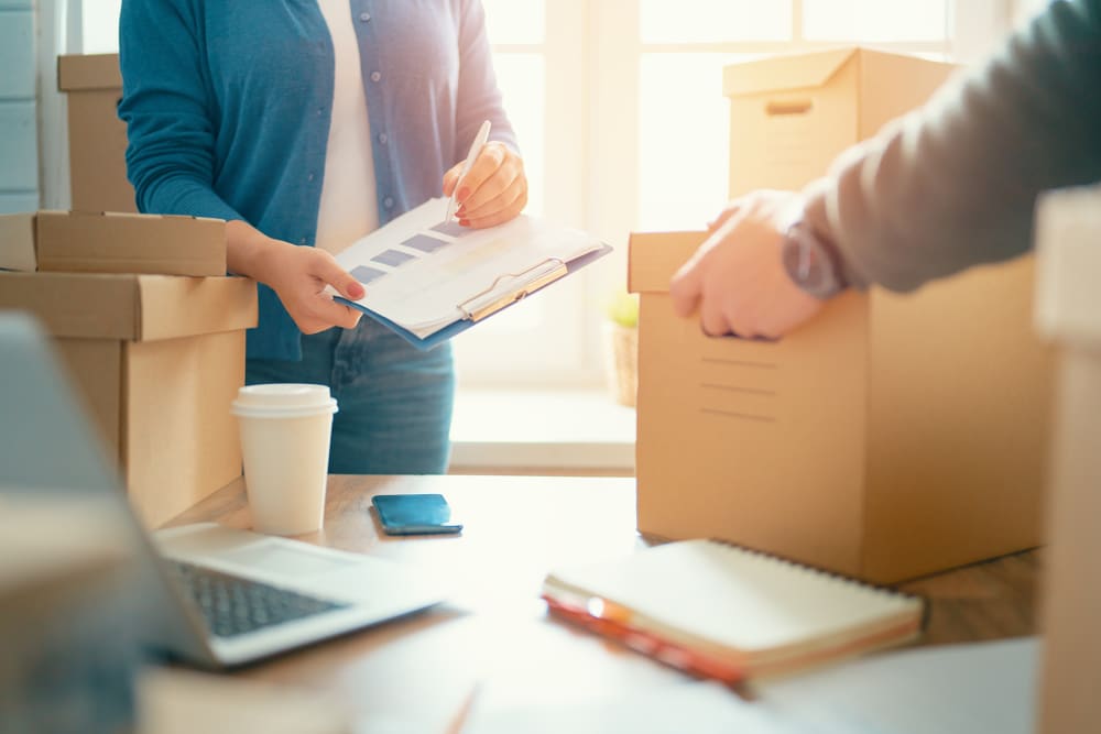 Woman holding a clipboard and man lifting a box from a table with business papers at A-American Self Storage in Honolulu, Hawaii