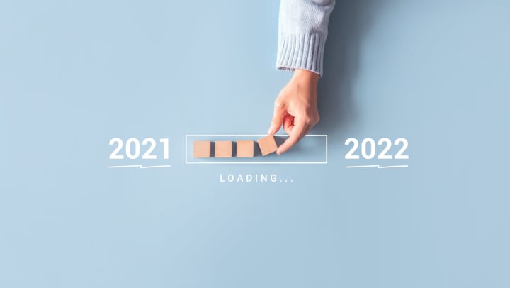 A hand places wooden cubes into a background illustration of a status bar as though loading a calendar from 2021 to 2022.