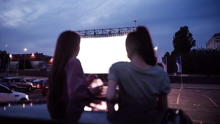 Two women sitting a car at a drive-in movie theater