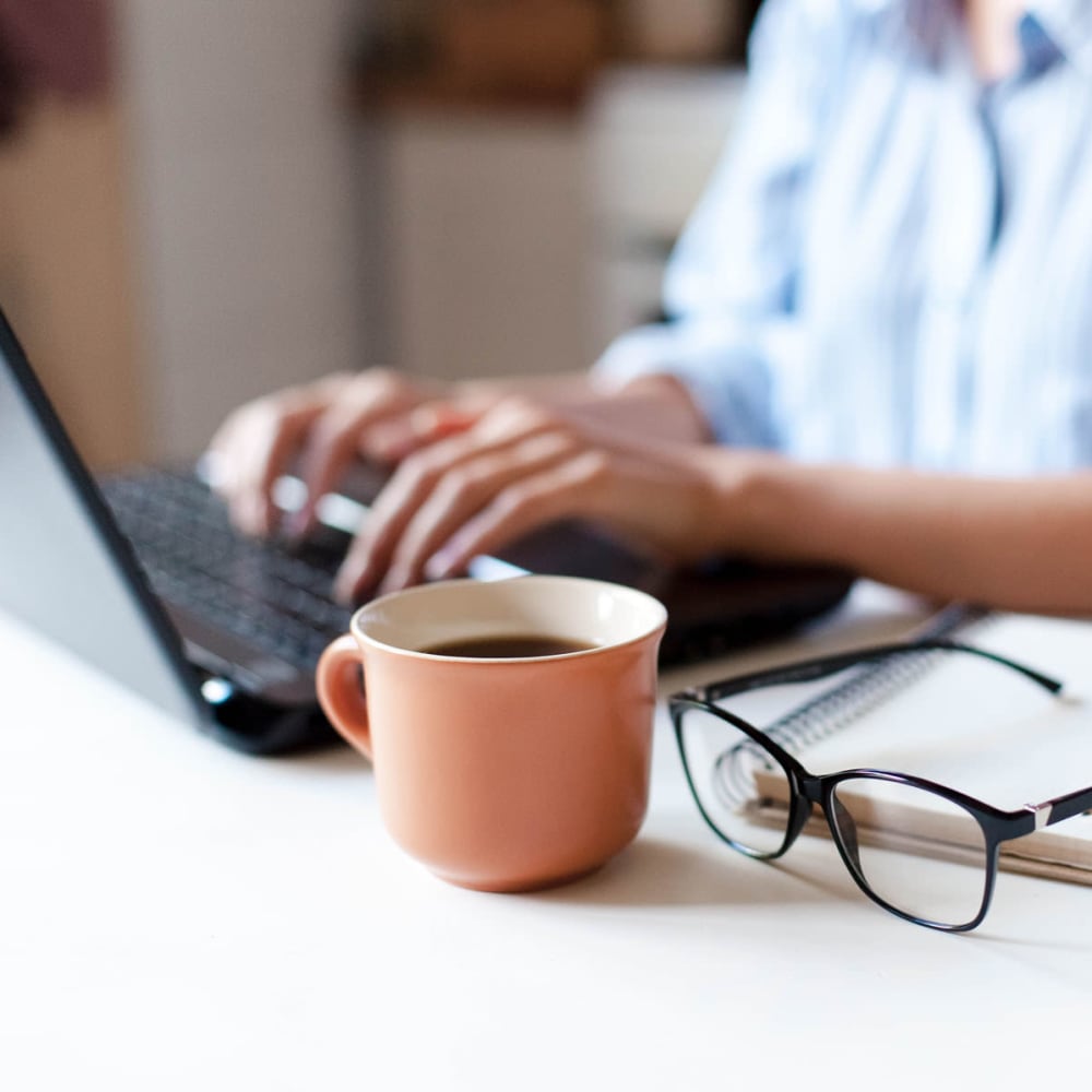 Resident using computer with coffee mug and glasses on desk