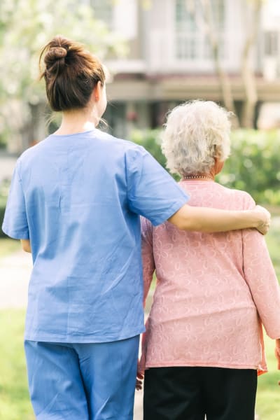 Memory care resident walking outside with a caretaker at Quail Park of Granbury in Granbury, Texas