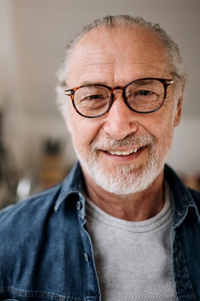Older man wearing a denim button down and tortoiseshell glasses smiling at Trustwell Living at Clyde Gardens Place in Clyde, Ohio