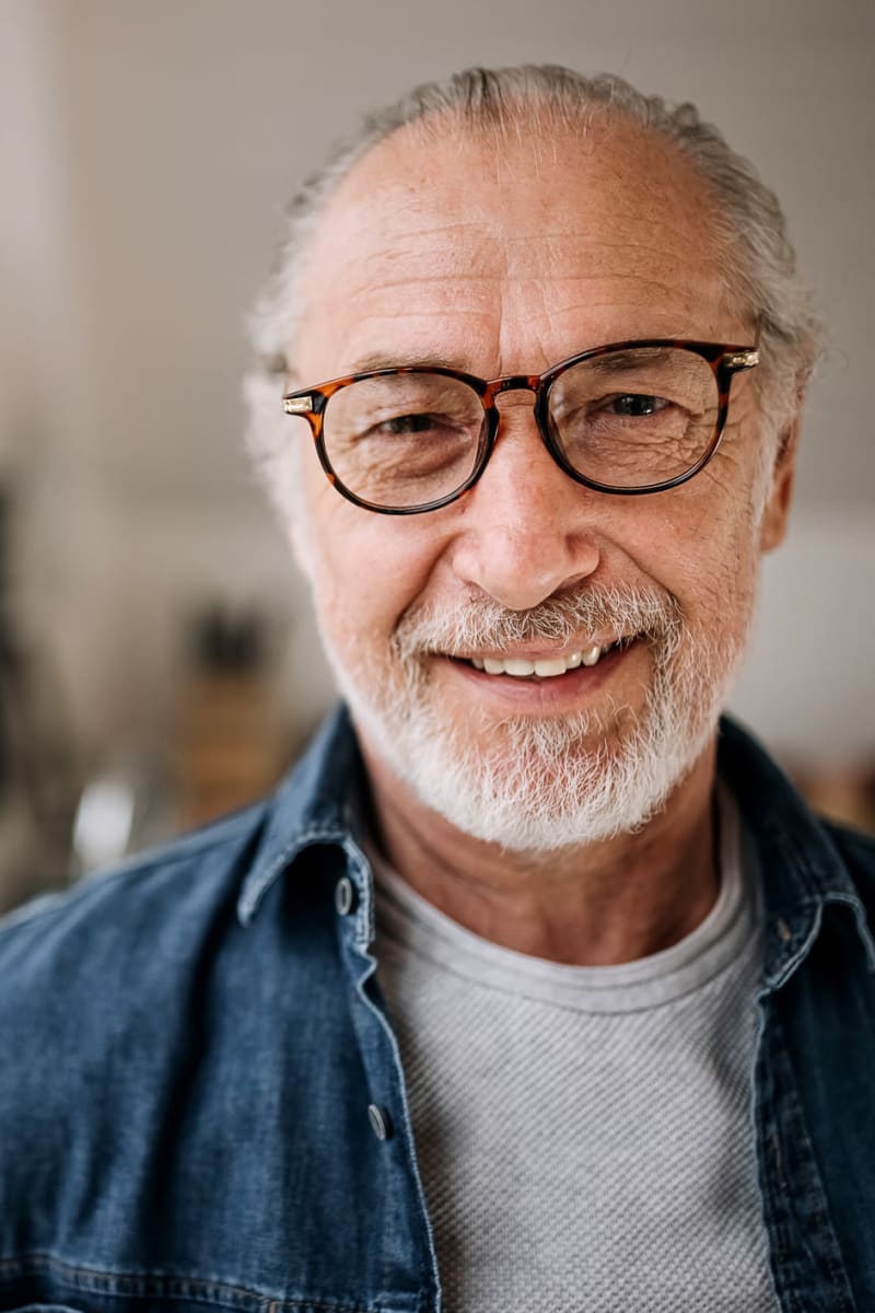 Older man wearing a denim button down and tortoiseshell glasses smiling at Trustwell Living at Ridgeview Place in Spokane Valley, Washington