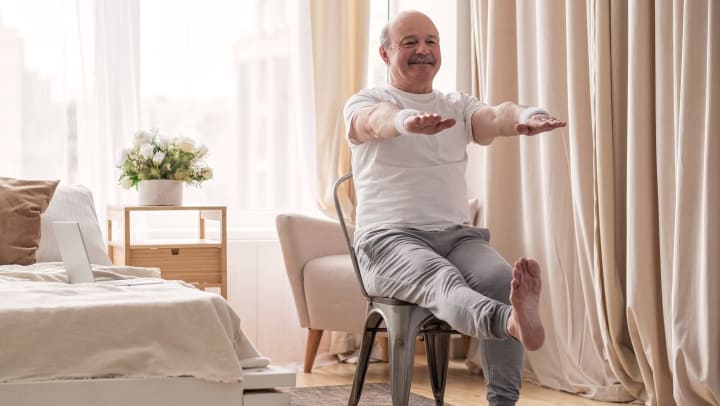 Elderly man practicing leg stretching while sitting in a chair
