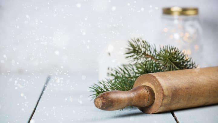 A rolling pin and tree needles on a table with a jar in the background