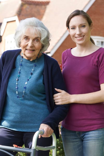 Resident walking outside with the aid of a caretaker at Quail Park Memory Care Residences of Visalia in Visalia, California