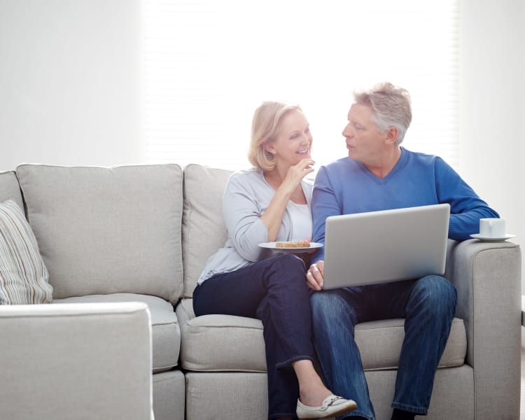 Older couple sitting on a gray couch together at Haddon Knolls Apartments